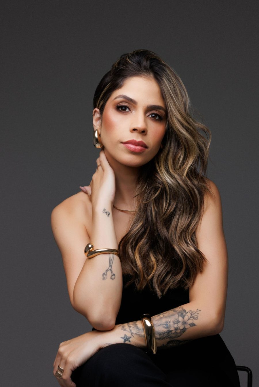Bruna Kimberlly sentada, com a mão no pescoço e uma tesoura tatuada no pulso