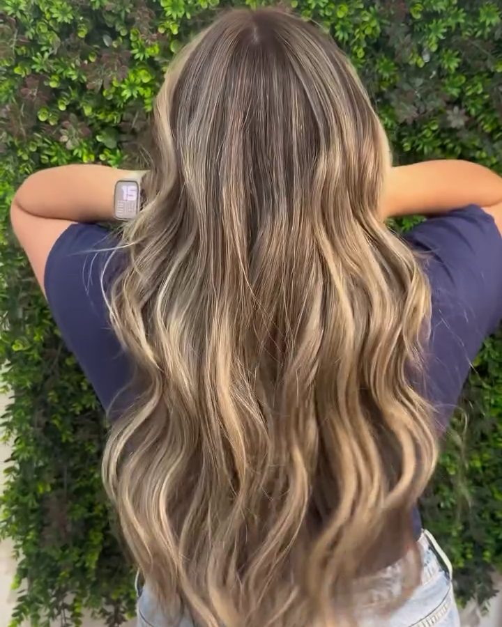 Depois: cabelo loiro iluminado em ondas, visto de costas, na parede verde do salão
