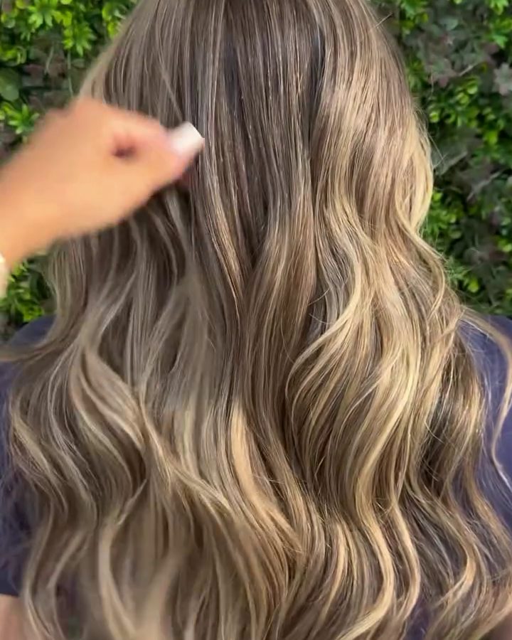 Mãos finalizando as ondas de um cabelo loiro iluminado no salão