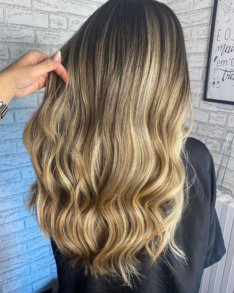 Cabelo com mechas mel feito no BK.HairPRO, diante da parede de tijolos brancos do salão